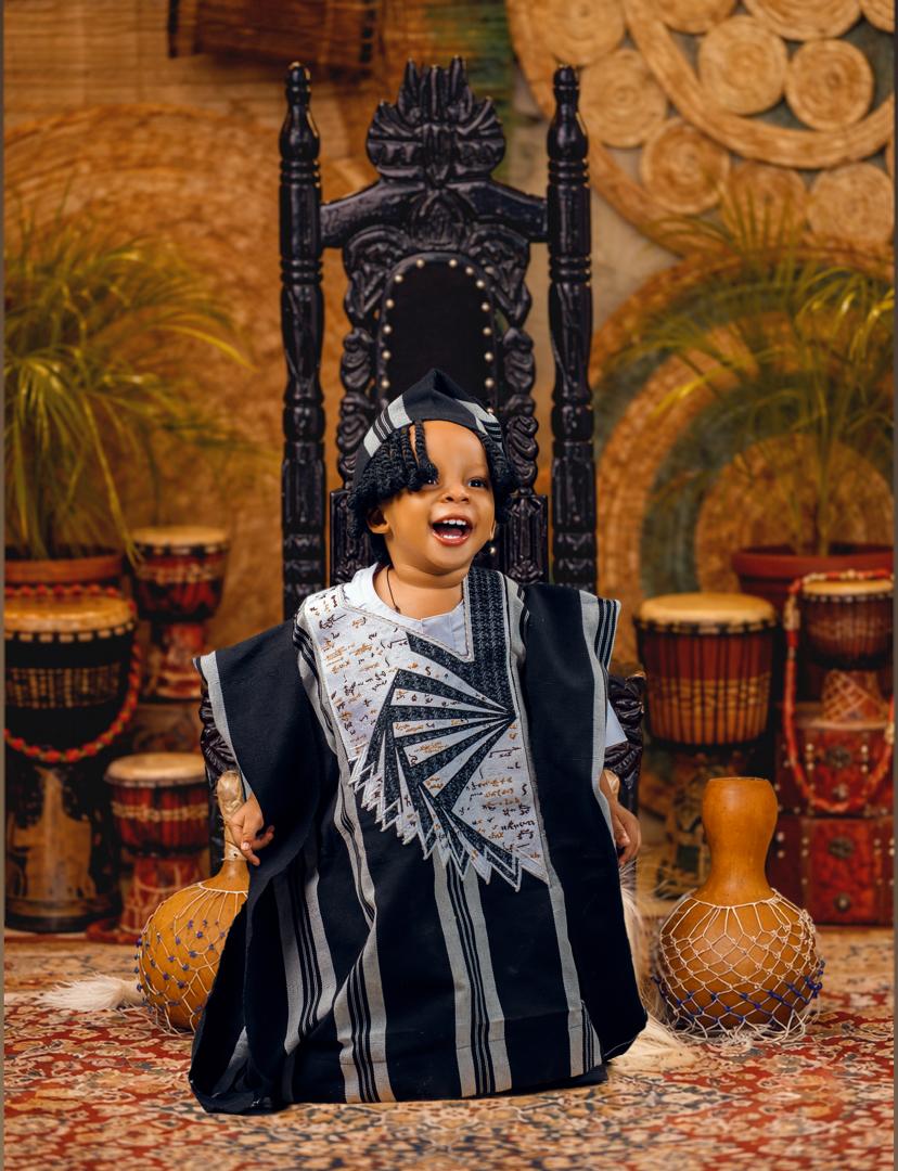 Boy in agbada seated on a carved throne with drums