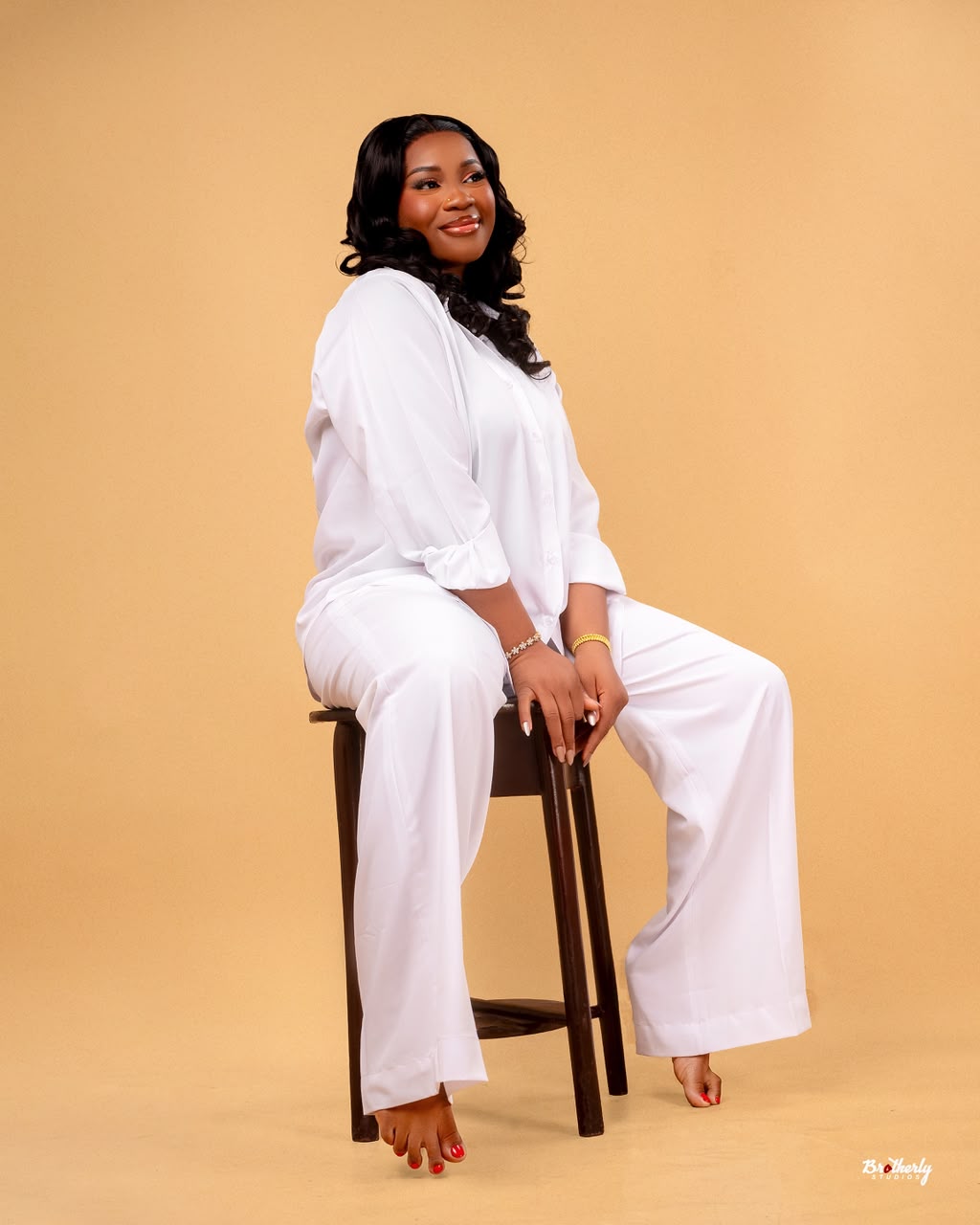 Woman in a white pantsuit seated on a wooden stool