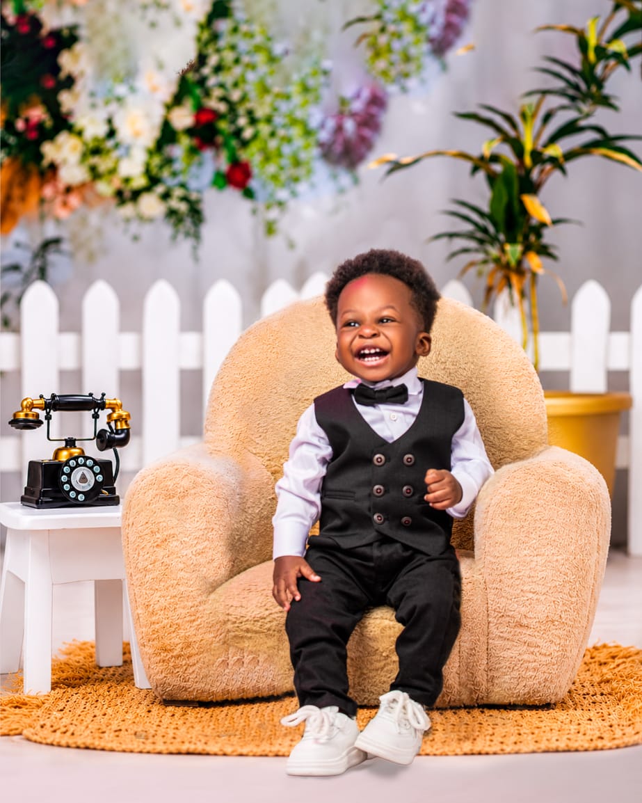 Toddler boy laughing in a three-piece suit on a plush armchair