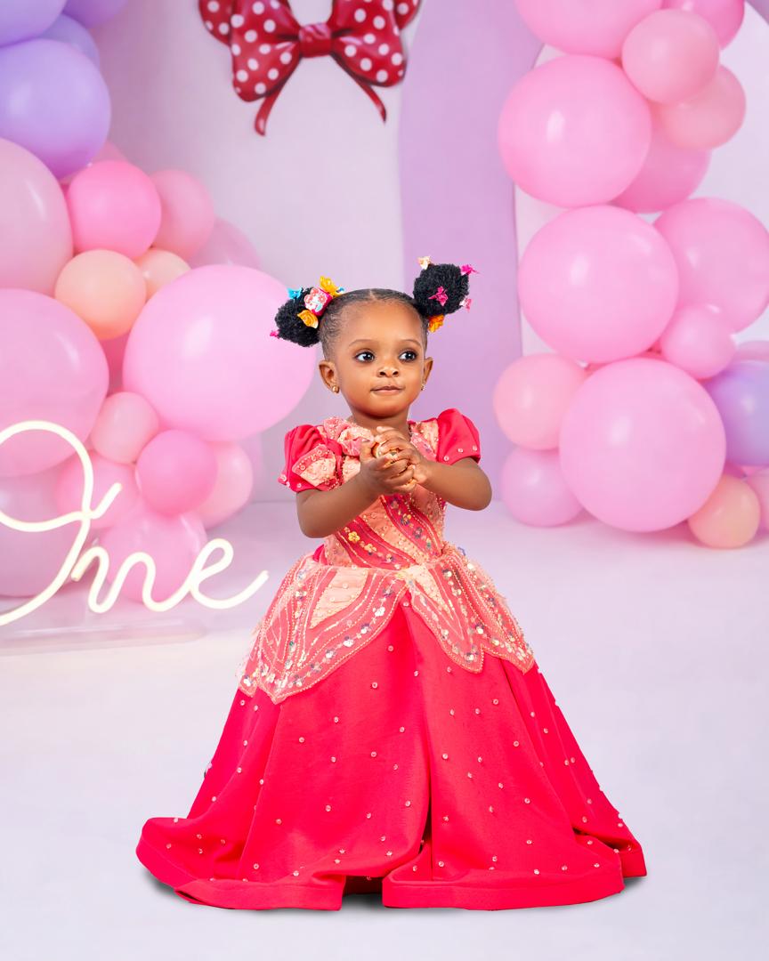 First birthday princess in a red dress beside a One sign