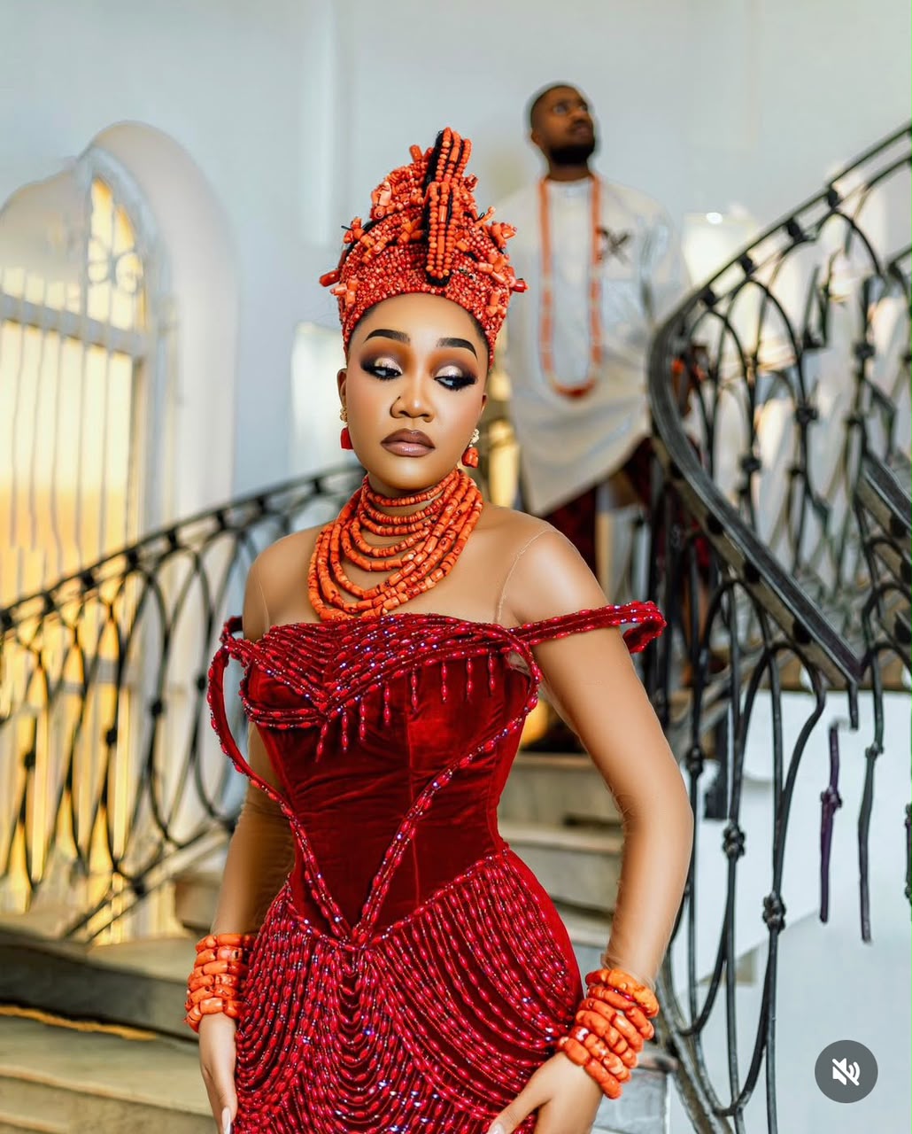 Traditional bride in red coral beadwork with her groom behind her