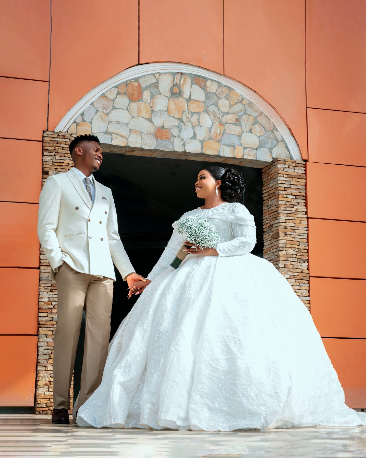 Bride and groom holding hands beneath a stone archway